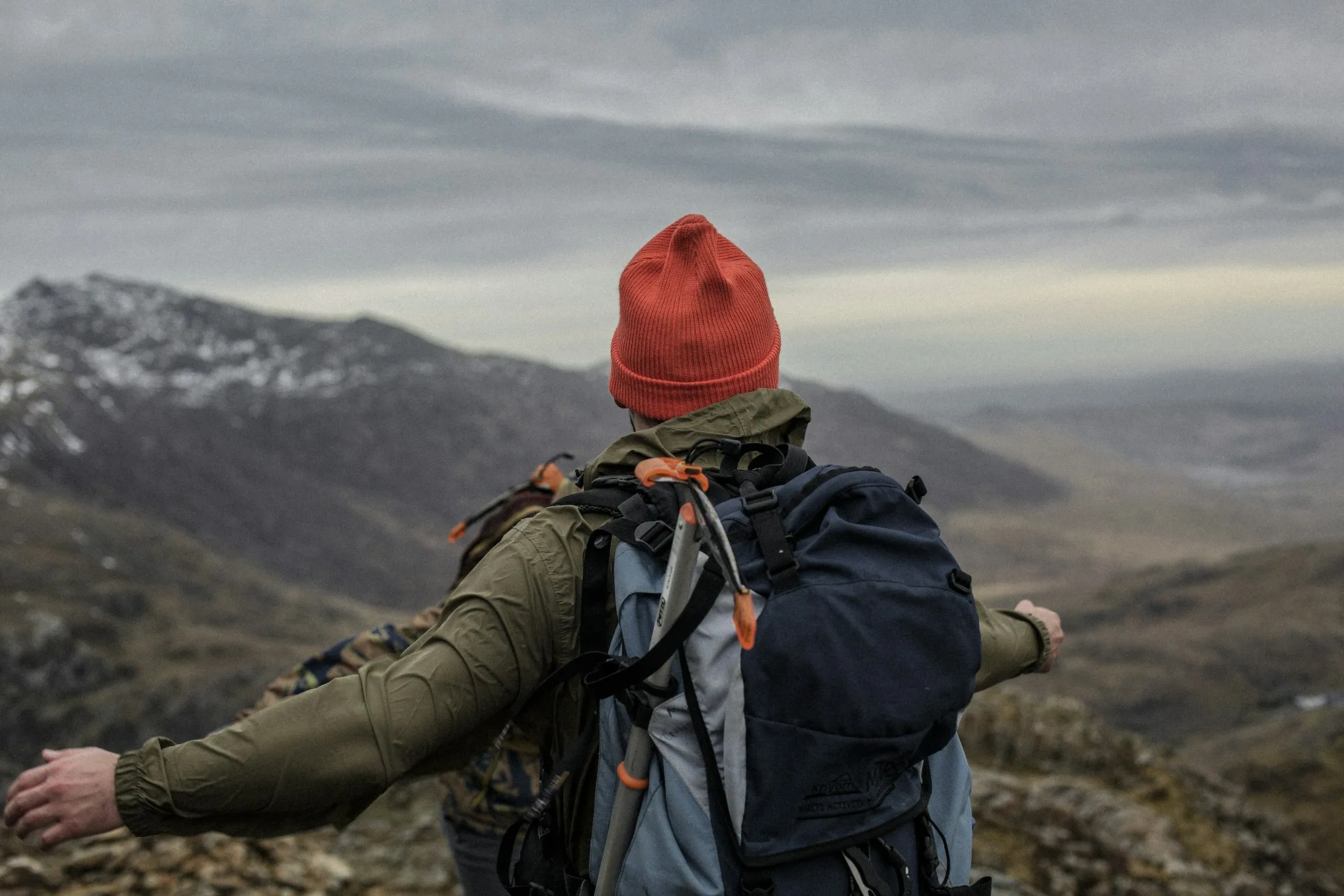 Jæger med orange strikhue og rygsæk ser ud over et bjergområde